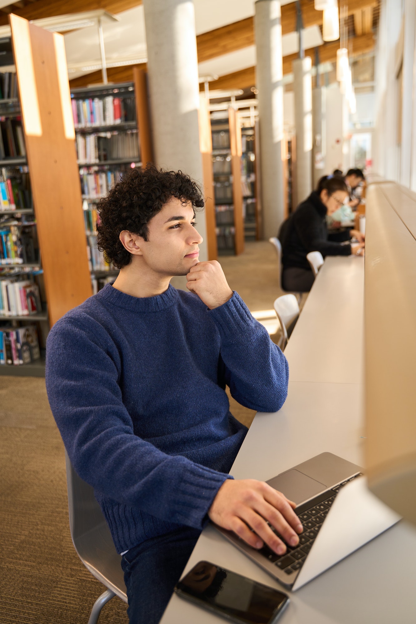 Smart mixed race male student online working, studying online in a modern library campus